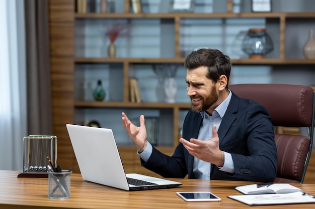 Angry and angry businessman talking on video call talking to colleagues and shouting quarrel mature