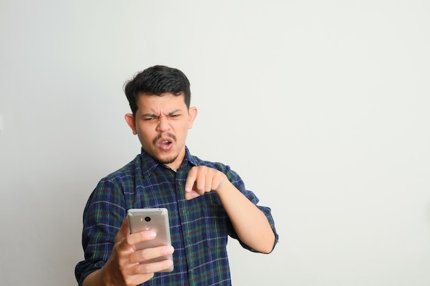 カジュアルなシャツを着た怒ったアジア人男性がスマートフォンで怒ります