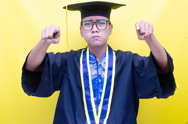 angry Asian man in graduation cap and gown shouting madly and showing disrespectful attitude