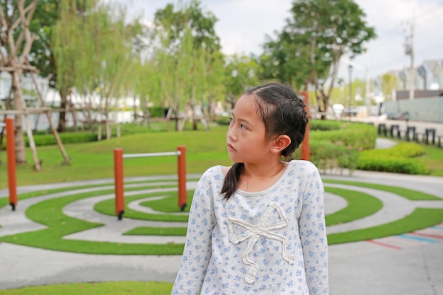화난 아시아 어린 소녀가 야외 정원에 앉아 옆을 바라보고 있다