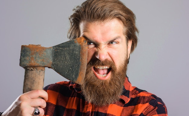 Angry bearded man with axe near face brutal canadian lumberjack with old ax closeup