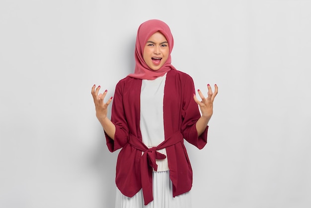 Angry beautiful Asian woman in casual shirt screaming out loud expressing negative emotions isolated over white background