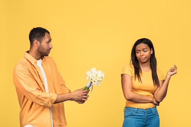 Angry black girlfriend rejecting flowers and apologies of her sad boyfriend after fight on yellow