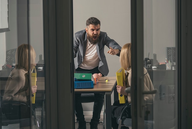 Angry boss blaming young woman with hands on face in office