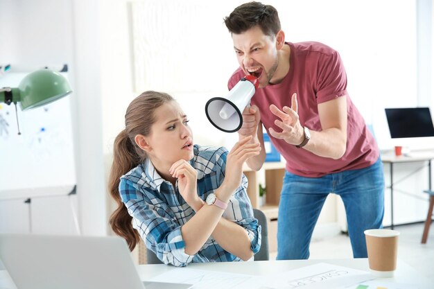 Angry boss with megaphone screaming at employee in office