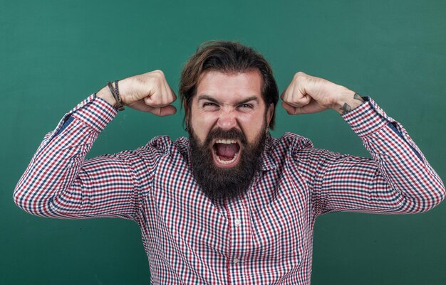 Photo angry brutal man work in classroom with blackboard prepare for exam college lecturer on lesson back to school formal education knowledge day mature bearded teacher at lesson