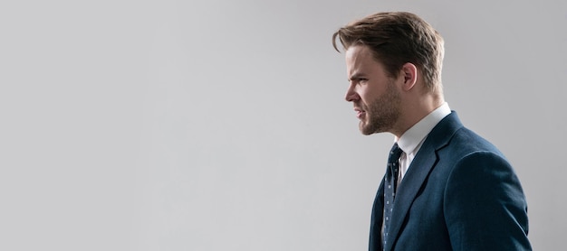 Angry business professional man stand sideway in anger grey background copy space boss Man face portrait banner with copy space Business man in suit isolated studio background banner poster