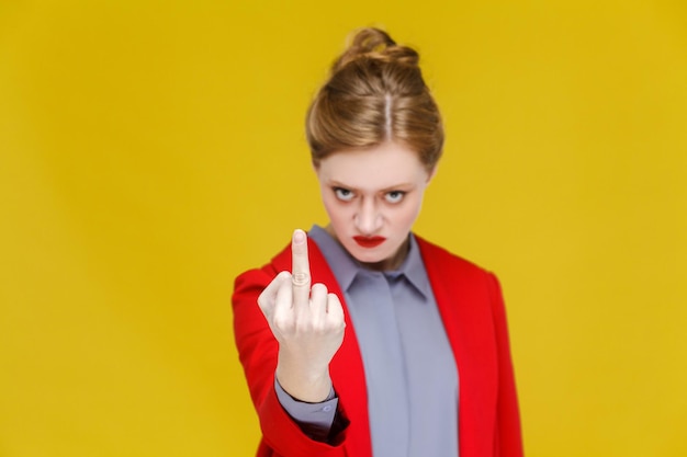 Photo angry business woman in red suit demonstrate fuck you sign. studio shot, isolated on yellow background