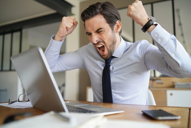 Uomo d'affari arrabbiato che perde pazienza e che grida al computer portatile in ufficio moderno