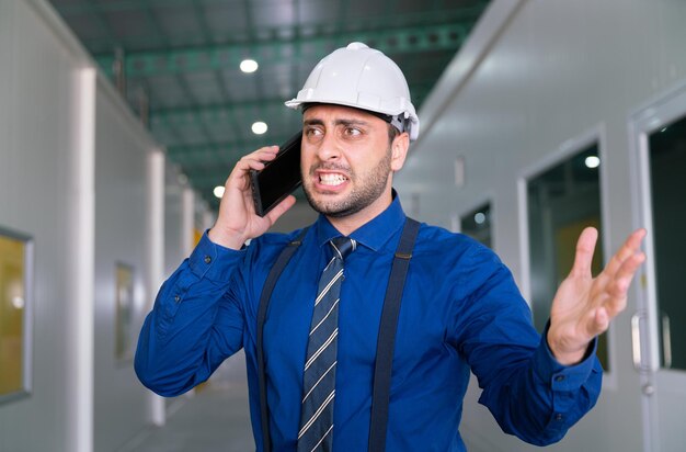 Фото Злой бизнесмен в костюме менеджера кричит о серьезном стрессе в офисе заводского склада с мобильного телефона