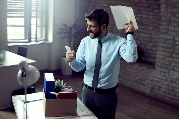 Angry businessman reading text message on mobile phone after being fired at work