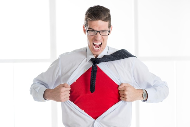 Angry businessman ripping open his shirt and exposing a Superhero red costume underneath. The man is wearing glasses and looking at camera.