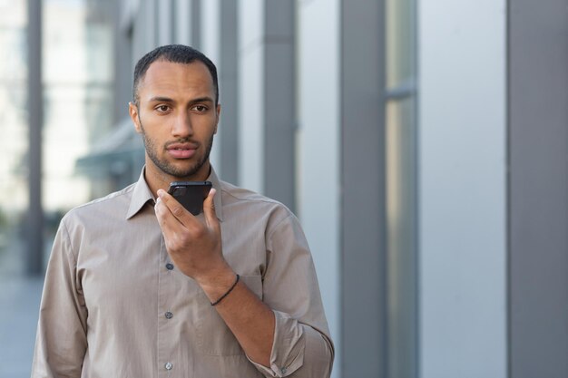 Angry businessman in shirt recording audio message from outside office building african american man