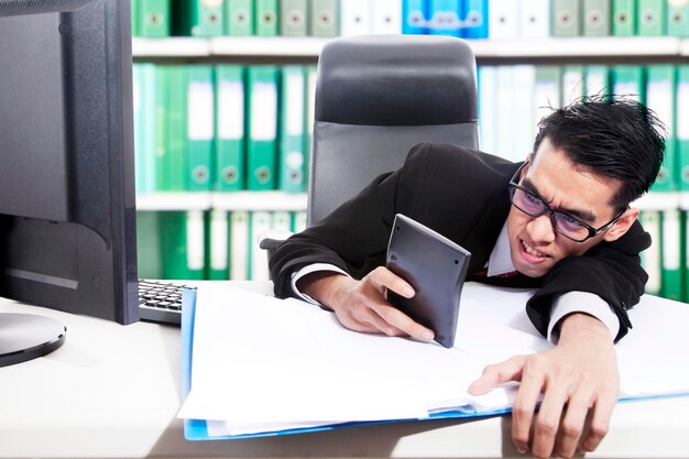 Angry businessman using calculator in office