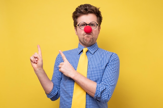 Angry caucasian man with red clown nose pointing aside with hand