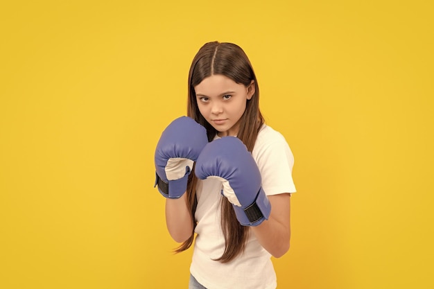 Angry child fighting in boxing gloves on yellow background