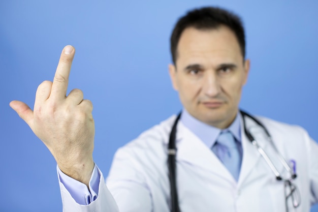 Angry doctor shows middle finger doing fuck you, rude attitude\
on blue