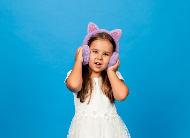 Angry emotional little girl in fur headphones on a blue background.