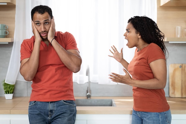 Photo angry evil aggressive young black wife scolding at offended husband suffering from pressure and stress