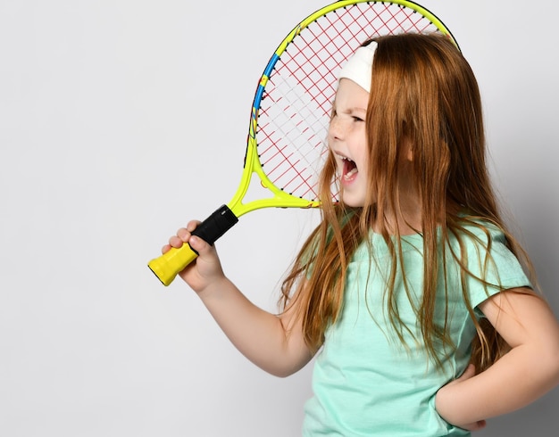 Foto ragazza malvagia arrabbiata grande giocatore di tennis headshot ritratto in studio isolato su bianco bambino sportivo furioso che tiene la racchetta gridando con rabbia frustrazione di perdere o gioco scorretto atteggiamento negativo