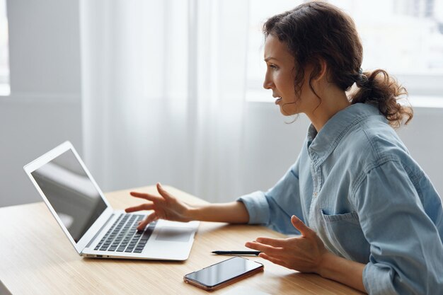 Angry evil pretty curly businesswoman worker screaming to
desktop raging after computer software crash error sitting at
workplace in home modern office technology gadget crash concept
copy space