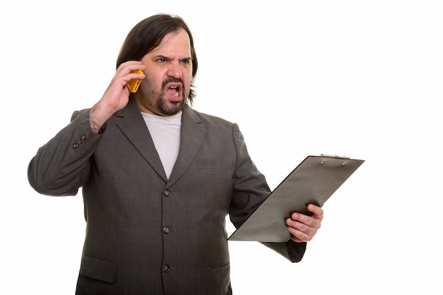 Angry fat Caucasian businessman talking on mobile phone while holding on clipboard