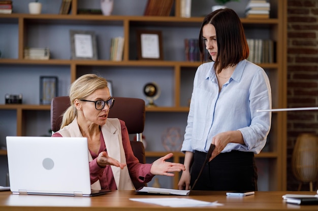 Photo angry female boss scolding sad and scared office worker demanding manager leader is annoyed at laziness and mistakes in paperwork of employee authoritarian leadership abuse of power