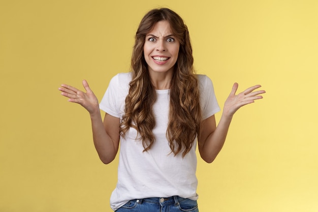 Angry freaked out disappointed woman frowning grimacing anger distress raise hands sideways full dismay complaining being rude arguing look pissed outraged swearing frustrated yellow background