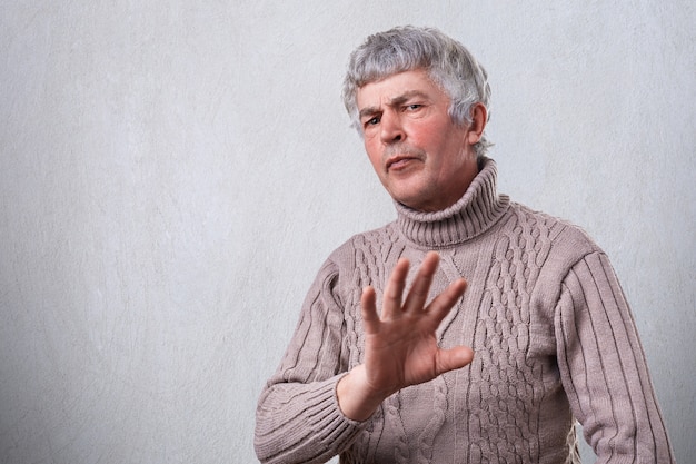 An angry frowning mature man having negative expression showing refusing sign with palm