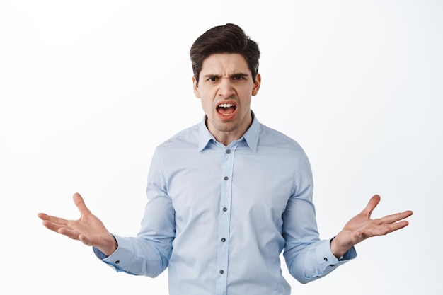 Angry and frustrated businessman, office worker complaining, look confused and displeased, arguing, standing against white background