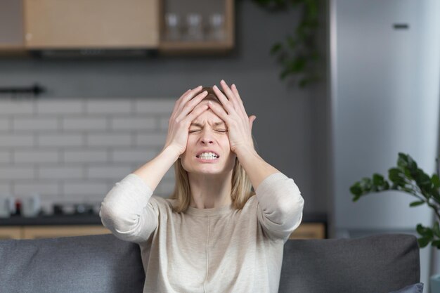 Angry and frustrated woman talking on video call looking at webcam angrily gesturing with hands while sitting on sofa at home