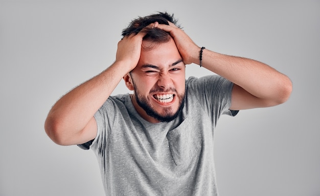 Angry and furious man on a gray background. He pulls out his hair in a rage