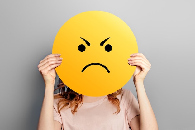 Foto angry girl heeft een gele smiley met agressief gezicht geïsoleerd op een grijze achtergrond