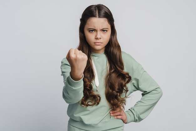 Photo angry girl shows fist, looks menacingly at the camera. little girl on a white background