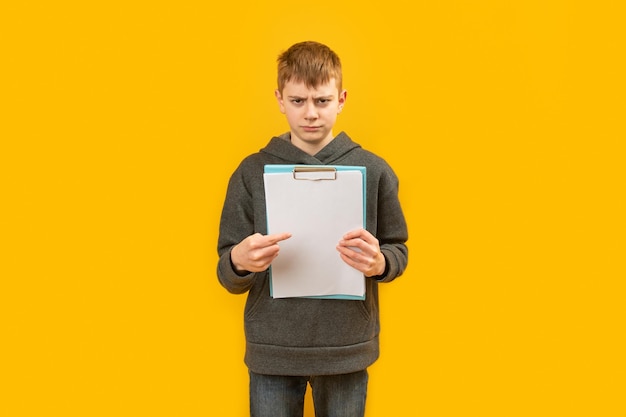 Angry gloomy boy in jeans and hoodie holds white sheet of paper and points his finger at it test results students assessment concept copy space