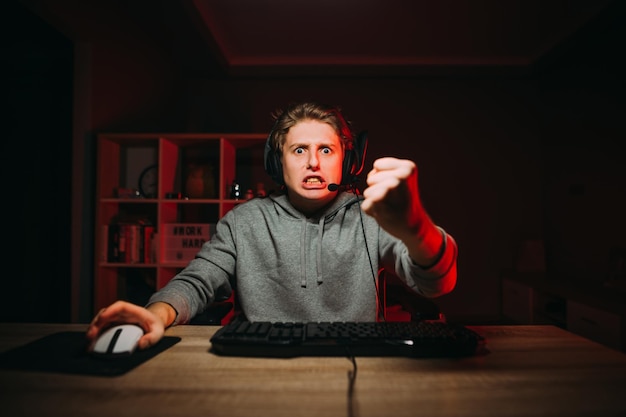 Angry guy gamer playing video games at night on the computer\
looking with a scary face