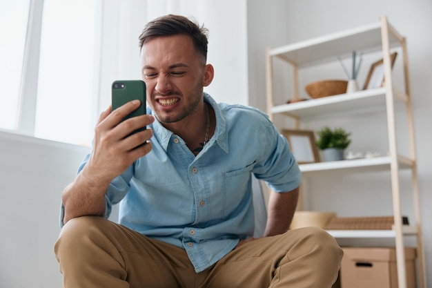 Angry irritated evil selfconfident handsome man tells with\
someone using video call at phone sitting at home attractive guy\
hates operation mobile crash problems time to buy new device\
concept