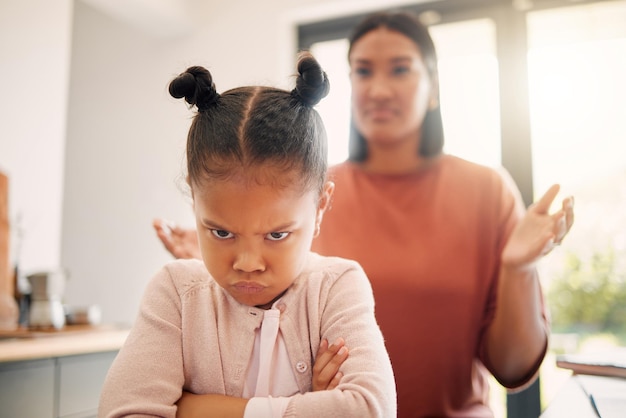 Photo angry little girl unhappy and upset after fight or being scolded by mother frowning with attitude and arms crossed naughty child looking offended with stressed single parent in background