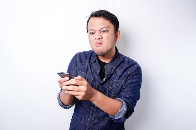 The angry and mad face of Asian man in blue shirt holding his phone isolated white background