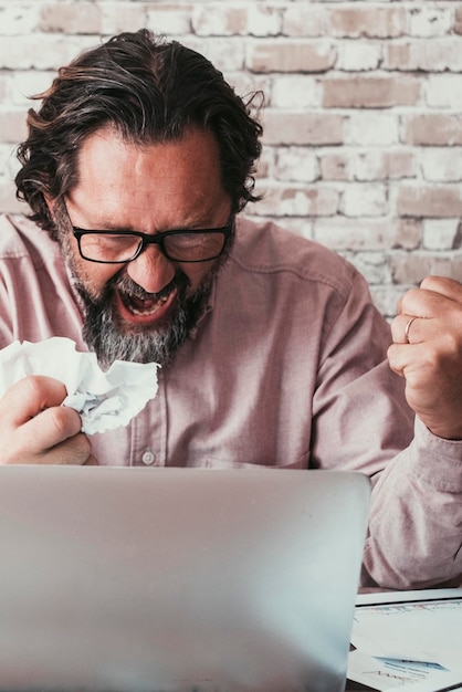 Angry man in bad expression looking a computer display with bad notifications Adult people working on line with stress and desperation emotions Front portrait of smart working adult male and laptop