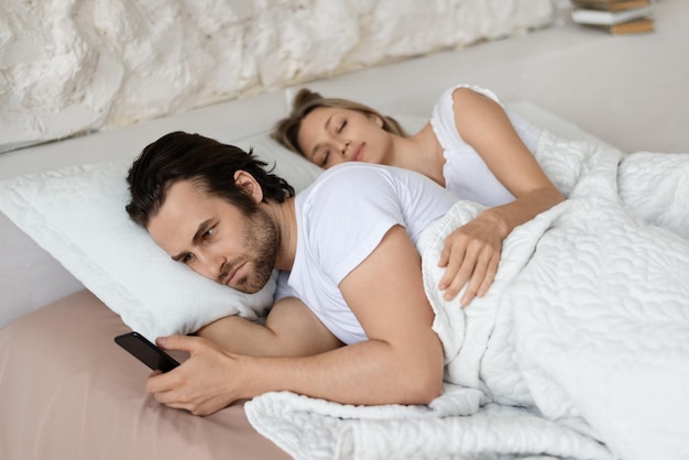 Angry man checking his sleeping girlfriend39s smartphone lying in bed at home husband feeling jealous