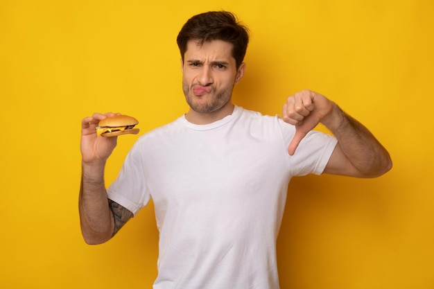 Angry man holding burger showing thumbs down