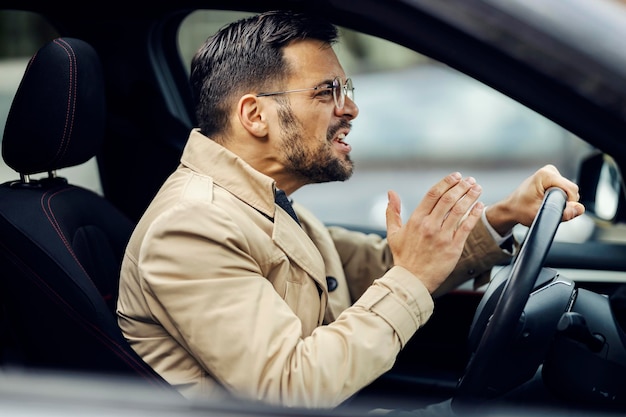 怒っている男が車に座って運転している間、他のドライバーを罵倒している