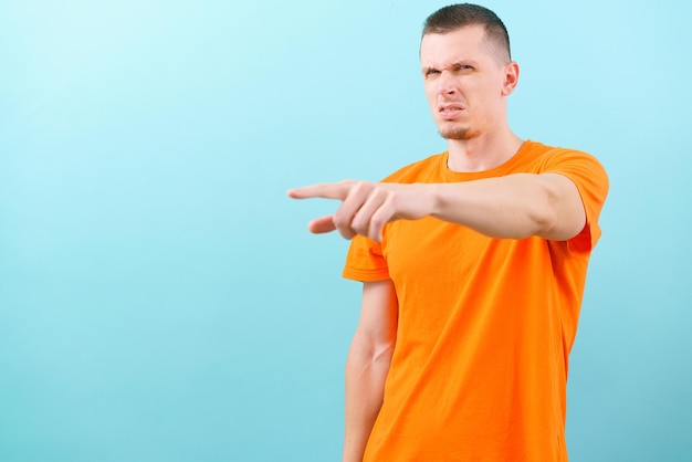 Angry man pointing the finger with an annoyed face on a blue\
background looking at the camera emotion gesture gesturing face\
hand attitude confident confused confusion crazy annoyed