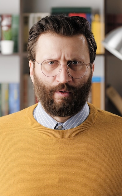 Uomo arrabbiato, rabbia. uomo barbuto infastidito arrabbiato con gli occhiali in ufficio o nella stanza dell'appartamento che guarda l'obbiettivo. vista ravvicinata