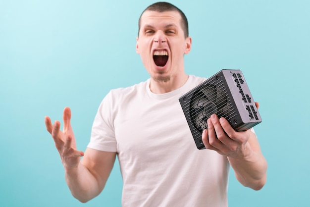 An angry man screaming and holding a computer power supply in his hand on a blue background Angry Crazy Inside Frustration Evil Engineering Mad Mouth Pc Device Person Voltage Cable