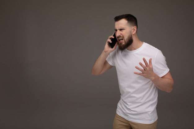 Злой человек кричит по телефону, изолированных на сером фоне