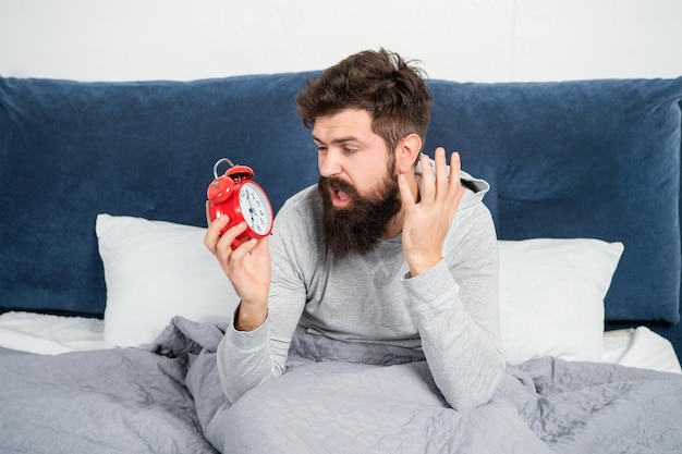 Angry man shouting at alarm clock being in bed awake in morning oversleep