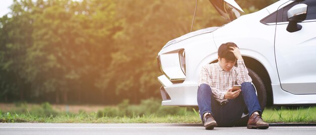 怒っている男は助けを求めて壊れた車の前に立つ