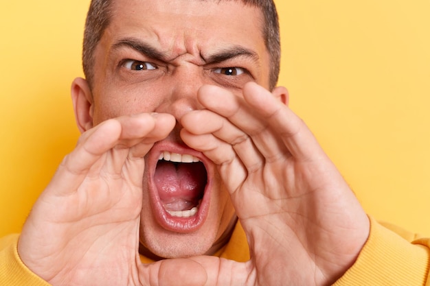 Angry man wearing casual style hoodie posing isolated over\
yellow background opens mouth widely screams in panic finds out\
horror news being in stressful situation